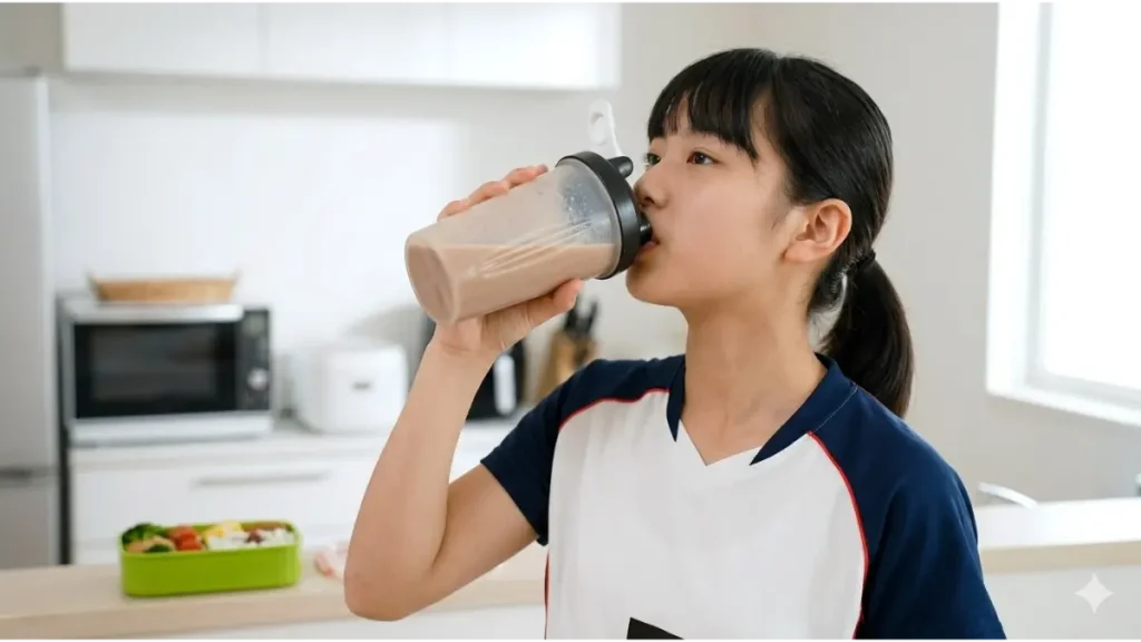 練習後に自宅キッチンでシェーカーボトルからドリンクを飲む、日本人中学生女子バレーボール選手。栄養補給を表現。