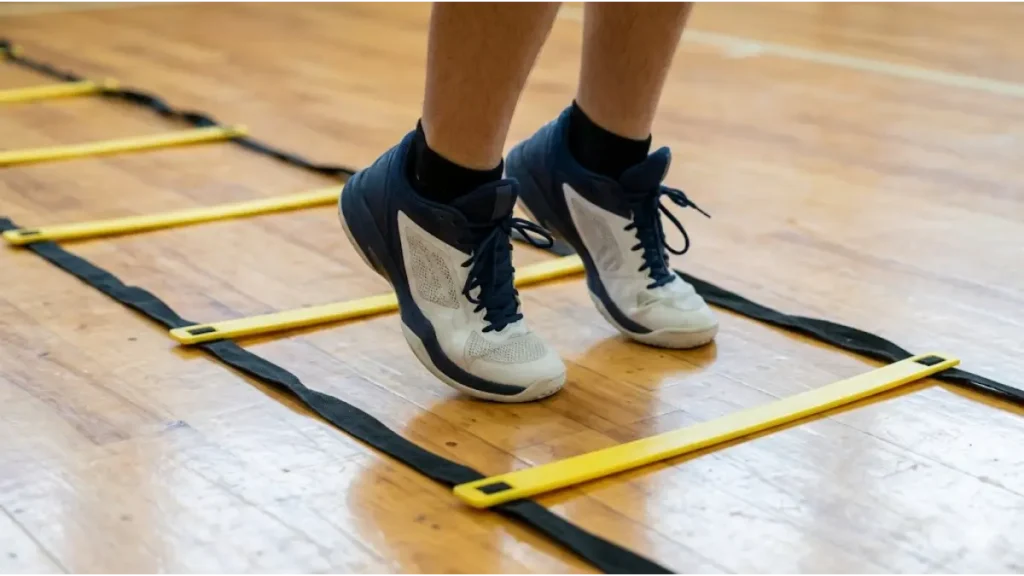 体育館の床で、黄色いアジリティラダーのマス目の中に、つま先（母指球）だけで立ち、かかとを浮かせた日本人男子高校生バスケットボール選手の足元のアップ。