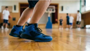 体育館の木製床にバッシュが擦れる瞬間と、遠くで練習するアジア人の生徒たちのバスケ部活動風景。