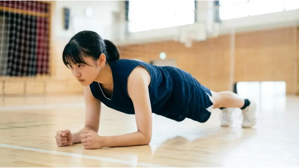 体育館の床で、怪我予防のために体幹トレーニングのプランクをする女子中学生バスケ部員。