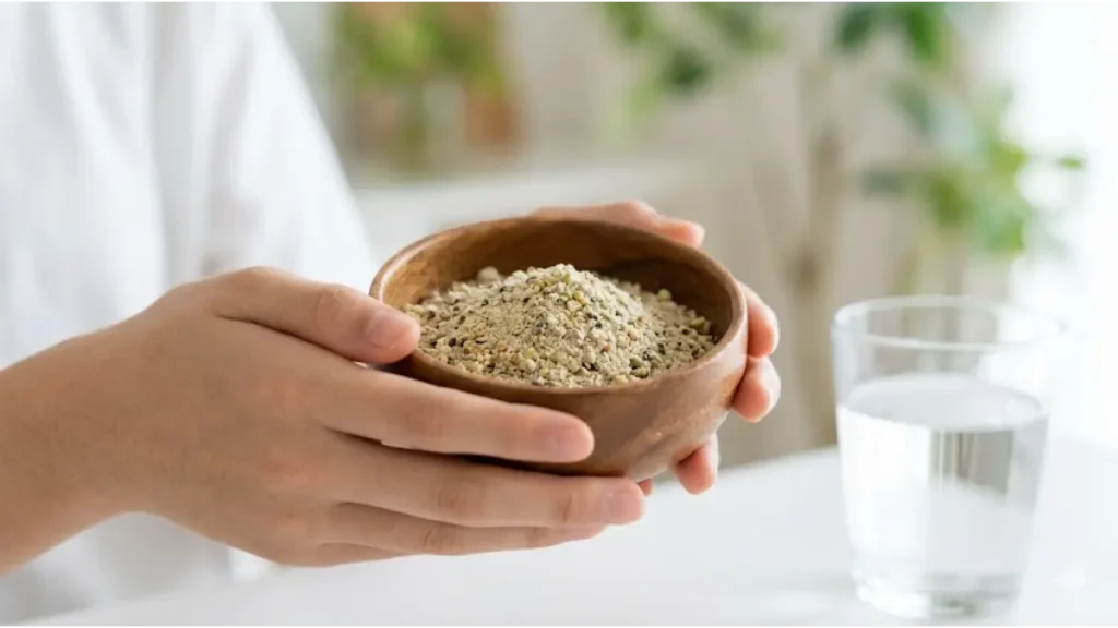 アジア人のティーンエイジャーの手元。木製のボウルに入った、微量栄養素（マグネシウム）を含むサプリメントパウダーと、その原料となるナッツや緑黄色野菜が少し見える。